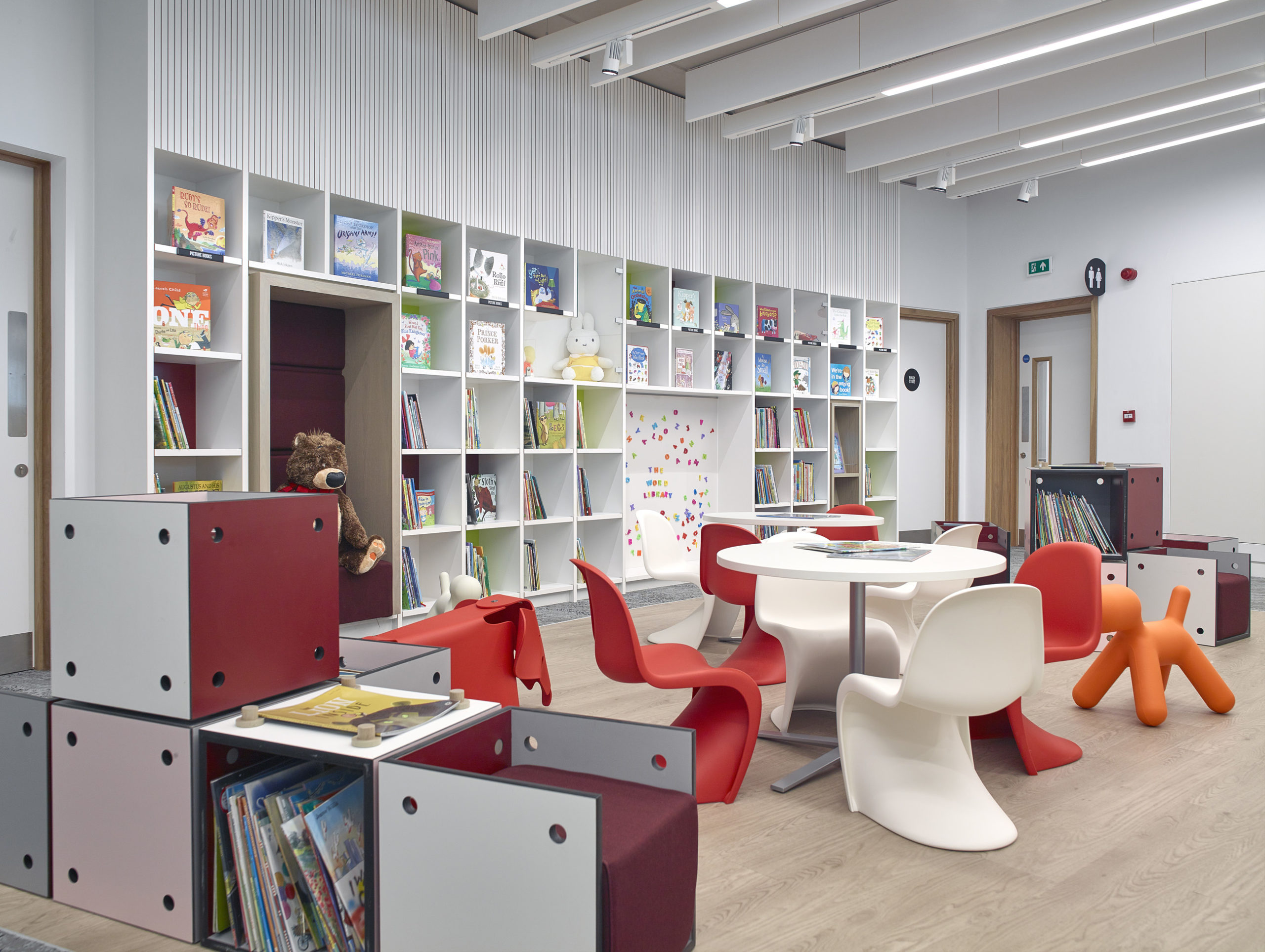 An interior with modern plastic furniture, bookshelves in coloured cubes and a large plastic orange dog.