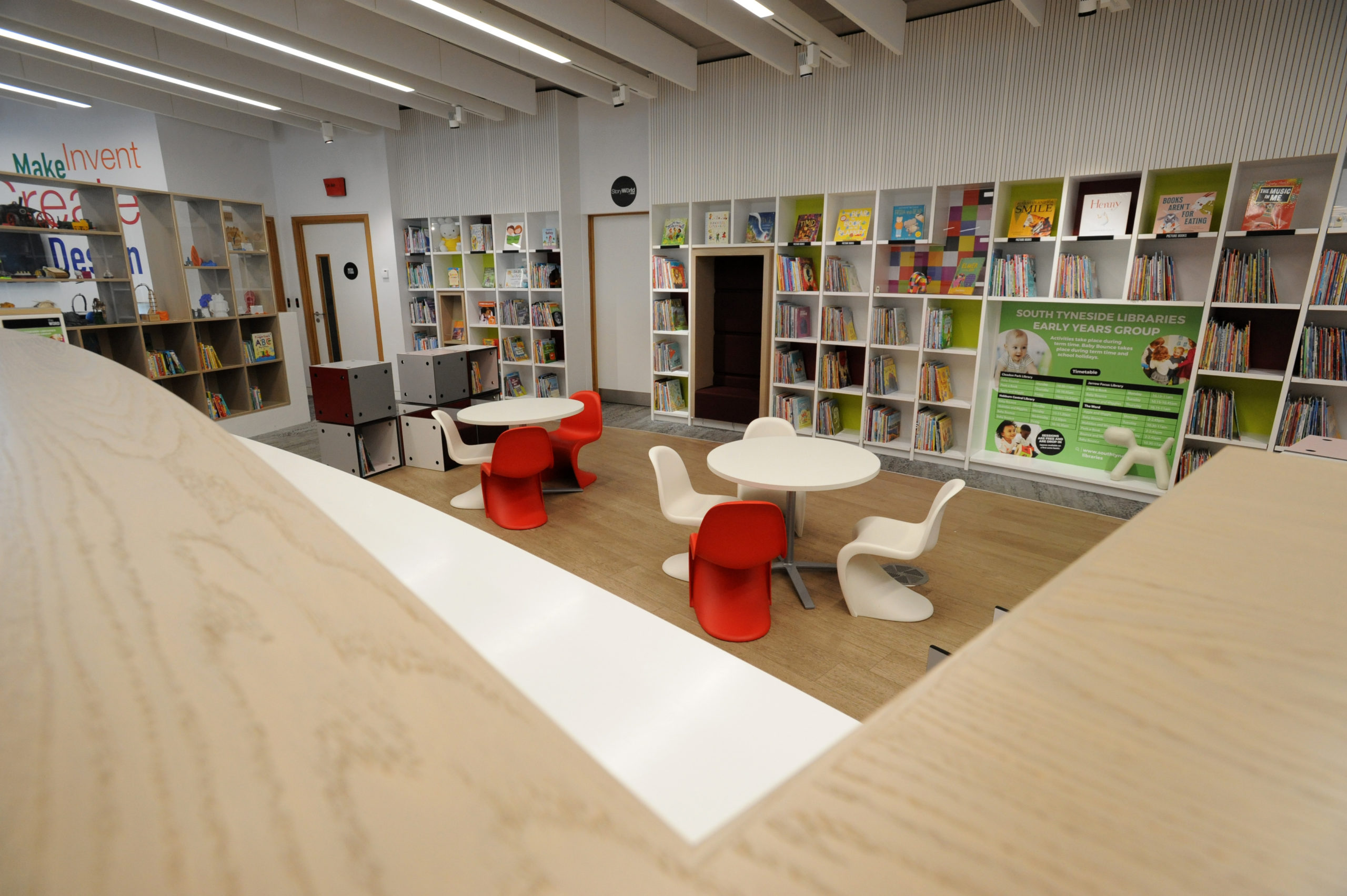 An interior featuring red and white plastic table and chairs and many bookshelves.
