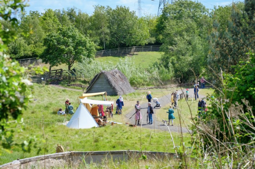 A small medieval village has been recreated in a green space at Jarrow Hall. People are wandering along a paved path beside two tents.