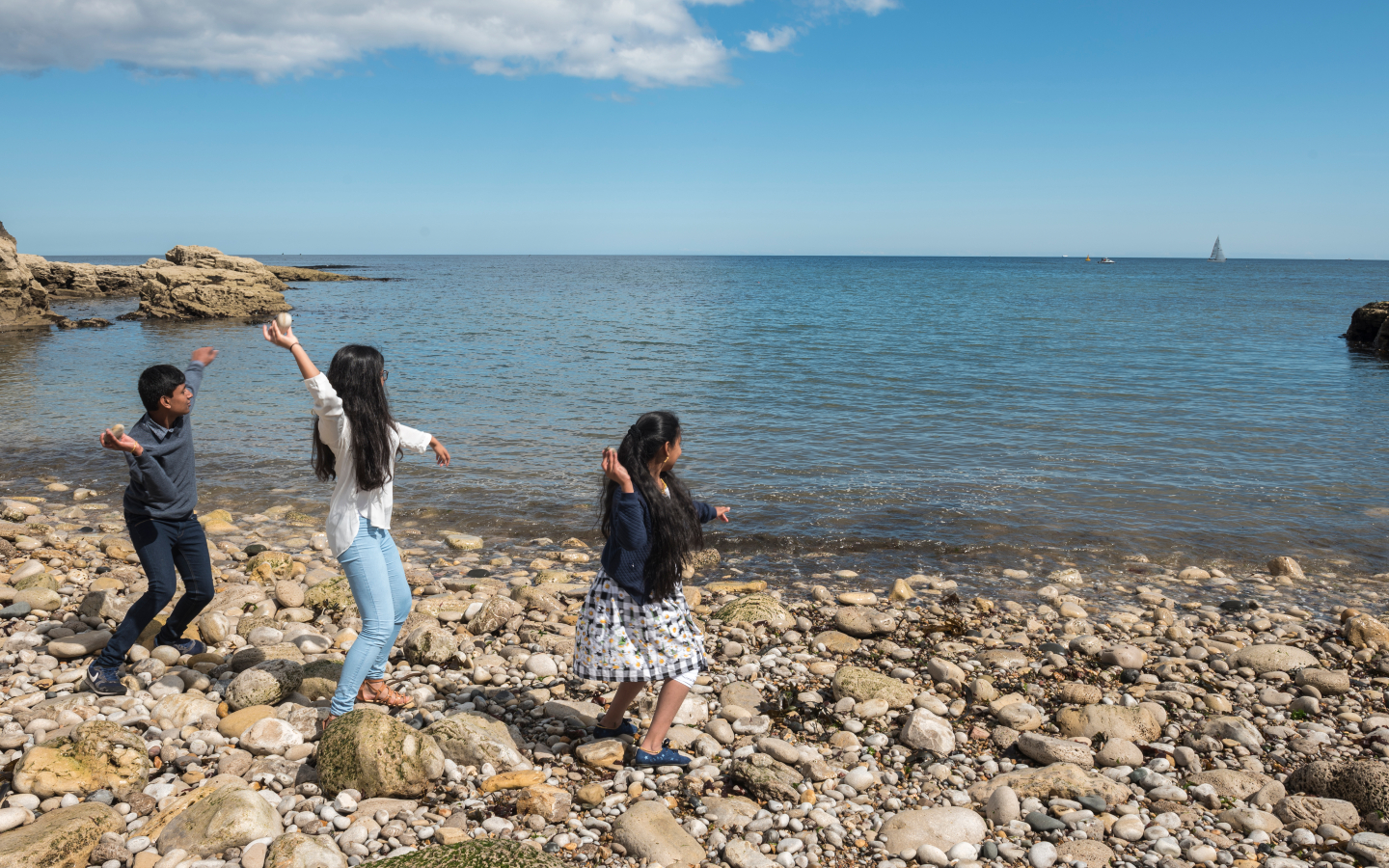 Two children on a rocky beach throw stones into the sea.