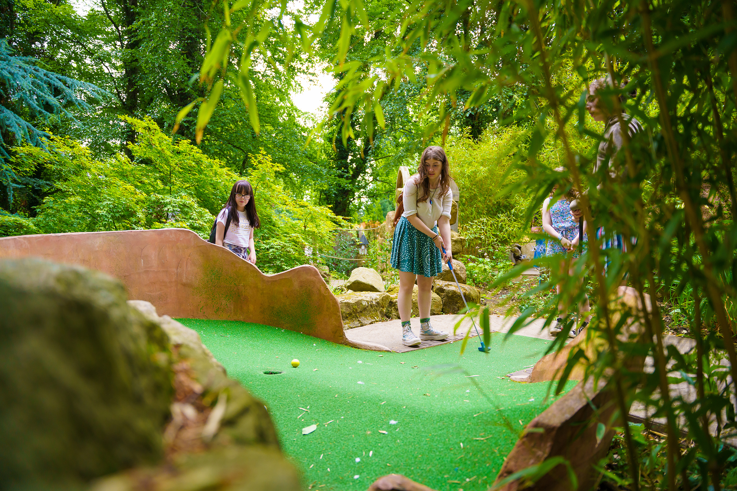 Two children playing golf in a woodland area.