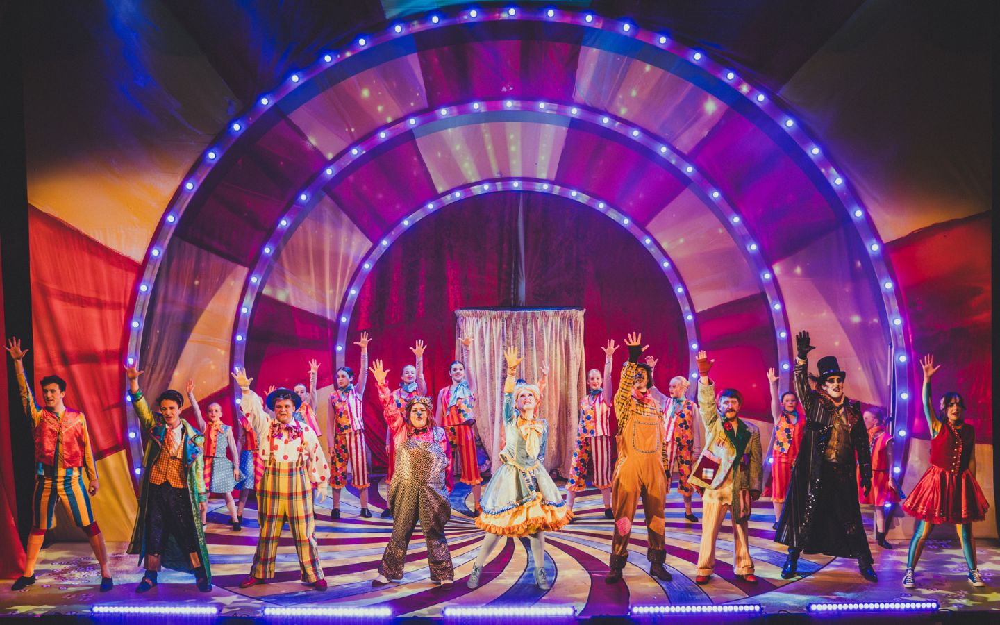 A colourful pantomime finale featuring costumed actors singing with their hands in the air.