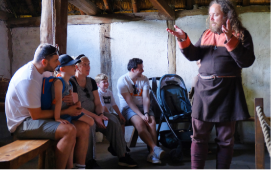 A storyteller dressed in Anglo Saxon clothing appears to tell a story to a smiling family.